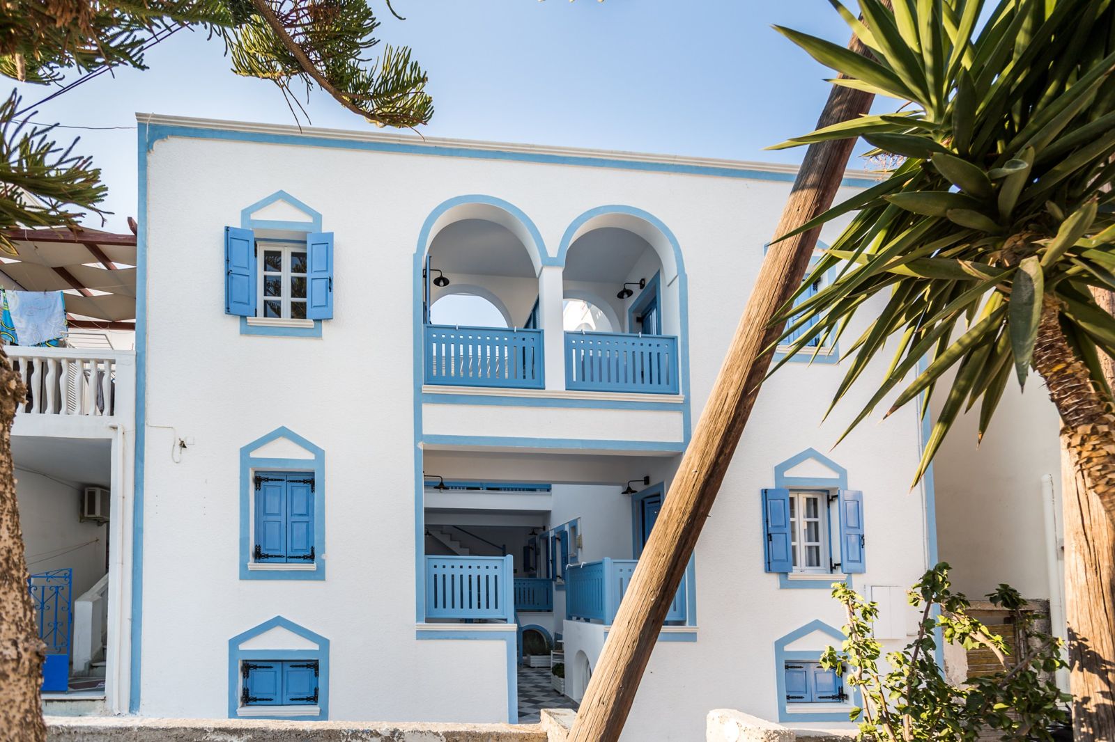 Whitewashed façade of Fanouris Condo in Kamari, Santorini, with blue shutters and twin arched balconies